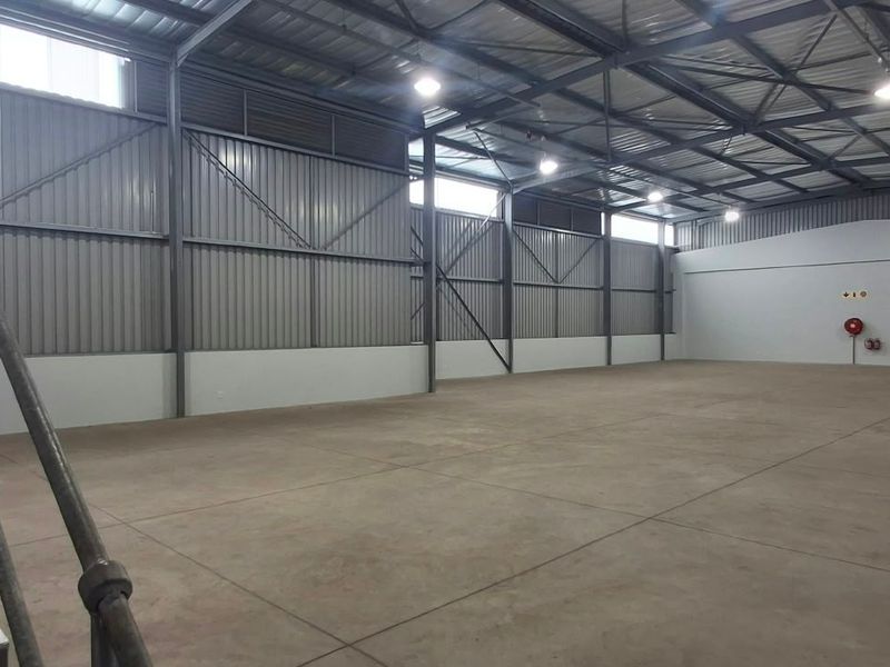 Spacious industrial warehouse unit featuring high ceilings with exposed steel trusses, concrete flooring, and a dedicated steel staircase.