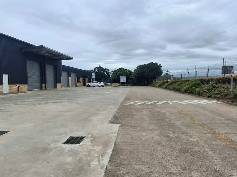 Industrial property exterior featuring a large concrete yard, multiple roller shutter doors, and secure perimeter electric fencing.
