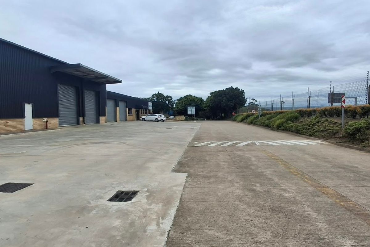 Industrial property exterior featuring a large concrete yard, multiple roller shutter doors, and secure perimeter electric fencing.