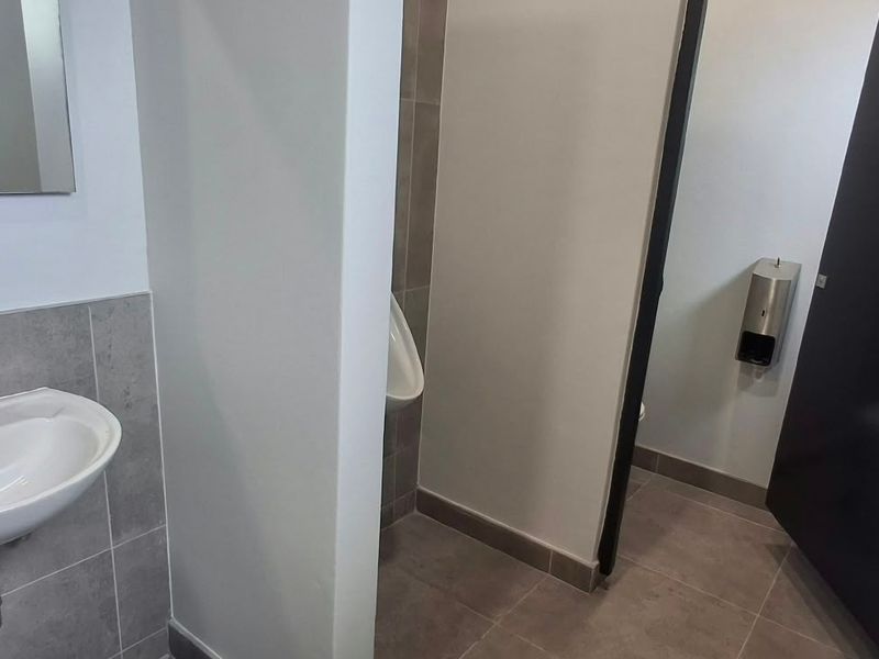 A clean, modern industrial-style restroom featuring a wall-mounted basin, tiled finishes, and a separate urinal area.