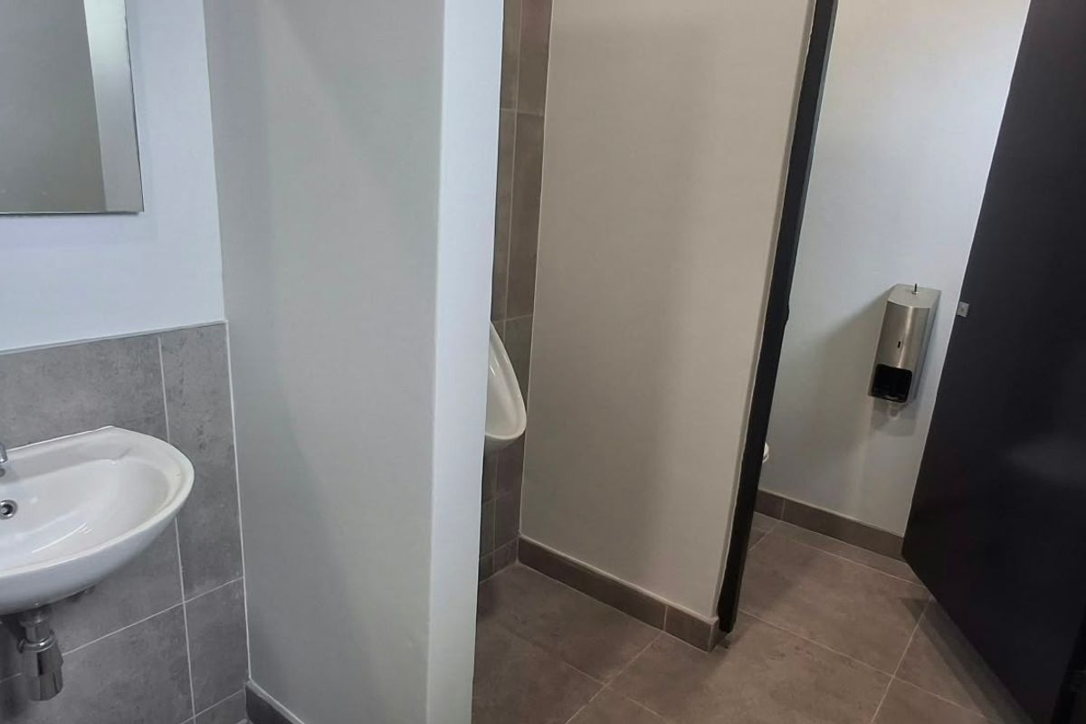 A clean, modern industrial-style restroom featuring a wall-mounted basin, tiled finishes, and a separate urinal area.
