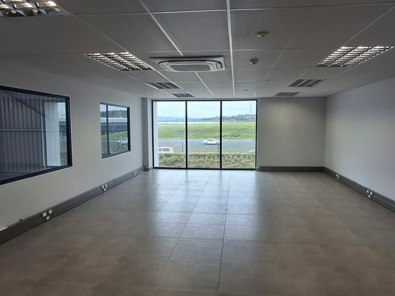 A spacious, modern, and empty office area featuring tiled flooring, recessed lighting, integrated air conditioning, and large windows providing natural light.