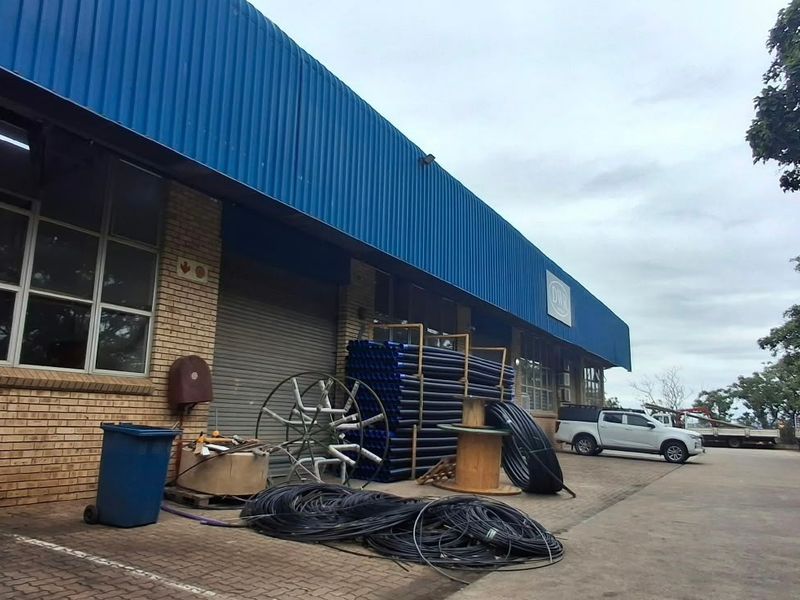 Industrial warehouse exterior featuring a blue corrugated metal roof, brick facade, and a roller shutter door with adjacent paved yard space.