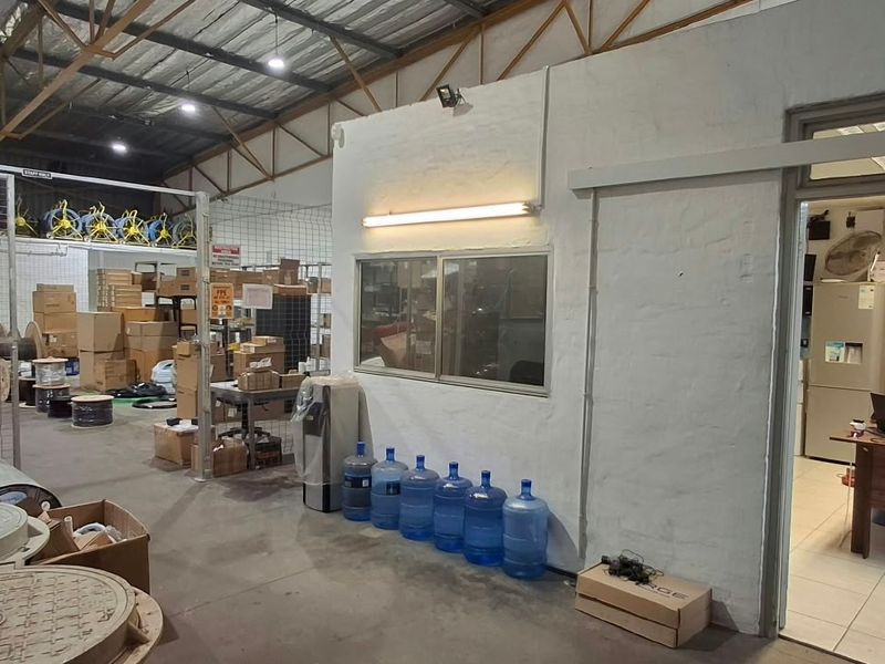 Industrial warehouse space featuring exposed steel roof trusses, concrete flooring, and an integrated office partition with internal window access.