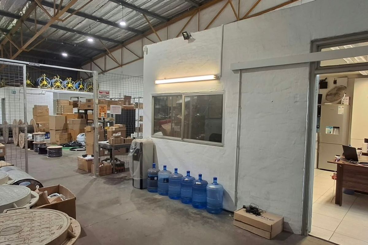 Industrial warehouse space featuring exposed steel roof trusses, concrete flooring, and an integrated office partition with internal window access.