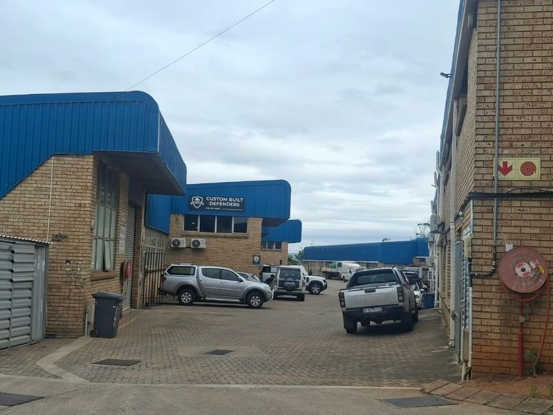 Exterior view of an industrial complex featuring face brick facades, blue corrugated metal roofing, and a paved driveway area.