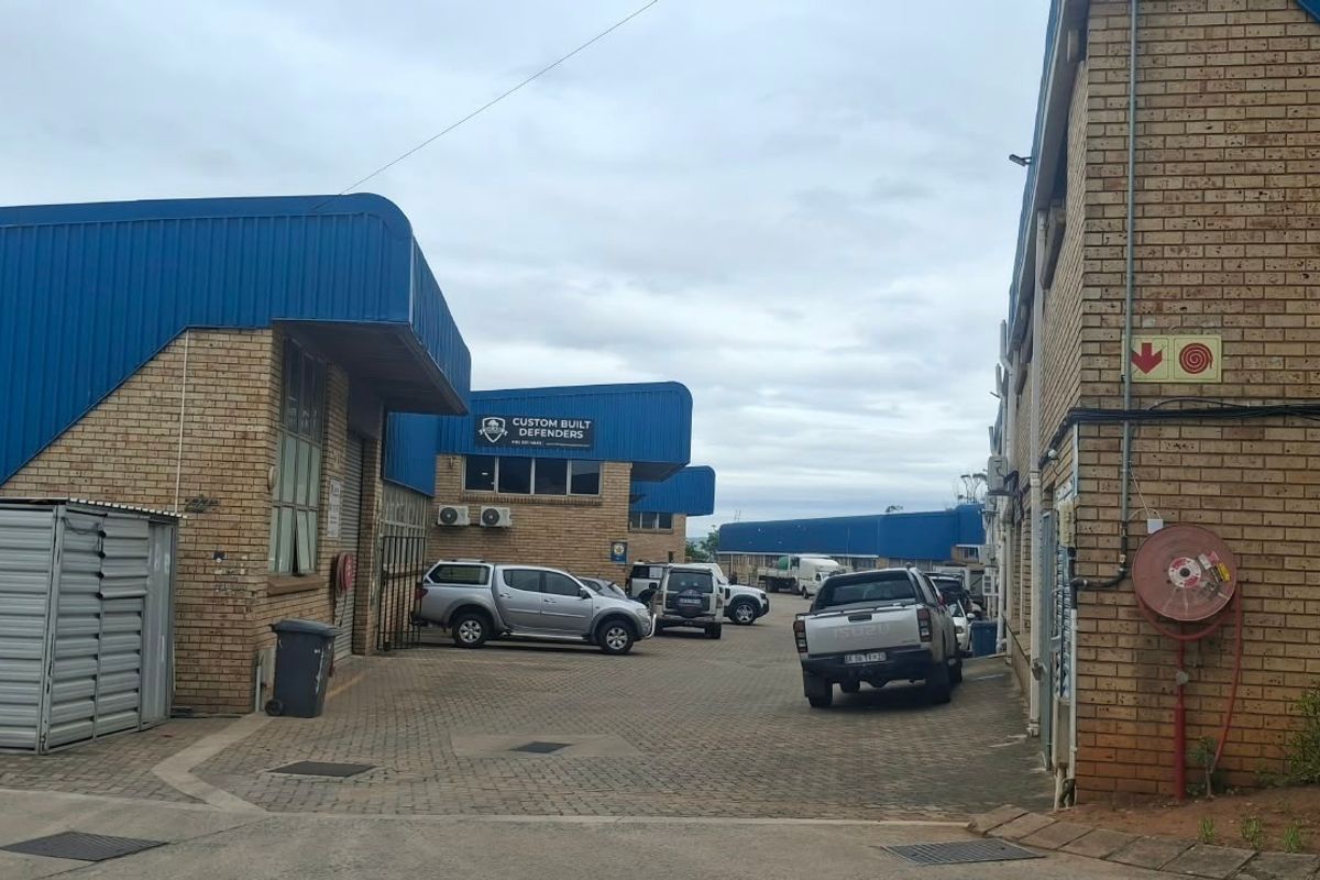 Exterior view of an industrial complex featuring face brick facades, blue corrugated metal roofing, and a paved driveway area.