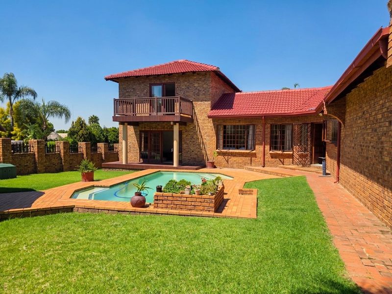 Rear view of the property featuring a swimming pool, brick-paved patio area, and a second-story balcony overlooking the garden.