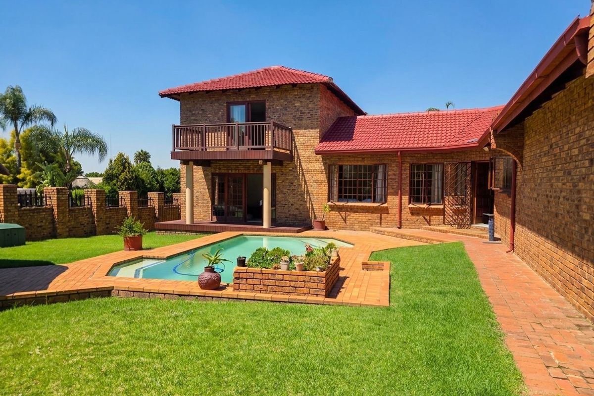 Rear view of the property featuring a swimming pool, brick-paved patio area, and a second-story balcony overlooking the garden.