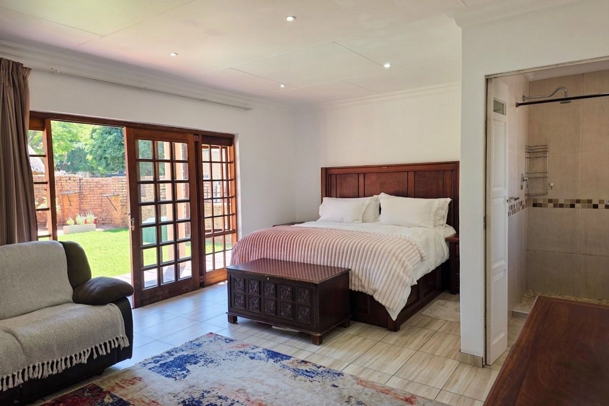 Spacious bedroom featuring tiled flooring, recessed lighting, and wooden sliding doors providing direct access to the garden, with an adjoining en-suite bathroom.