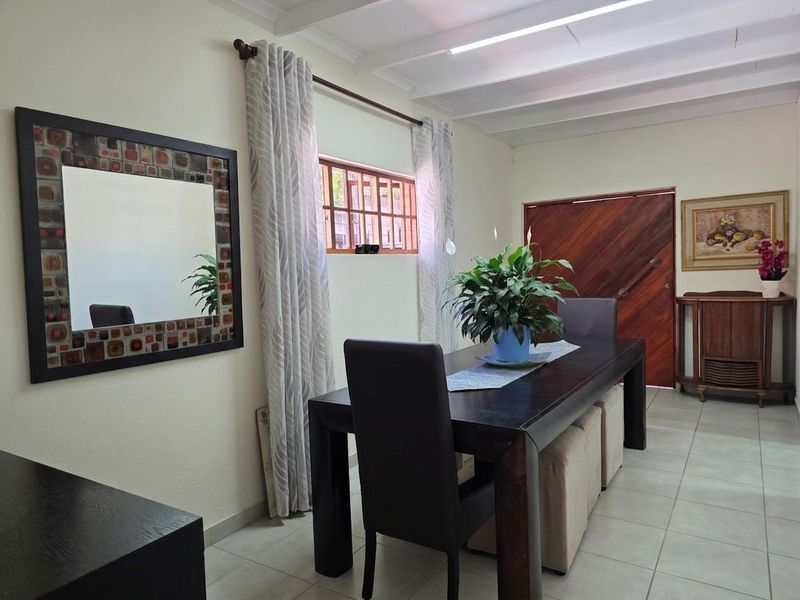A dining room featuring tiled flooring, exposed beam ceilings, and a solid timber entrance door with security-barred window.