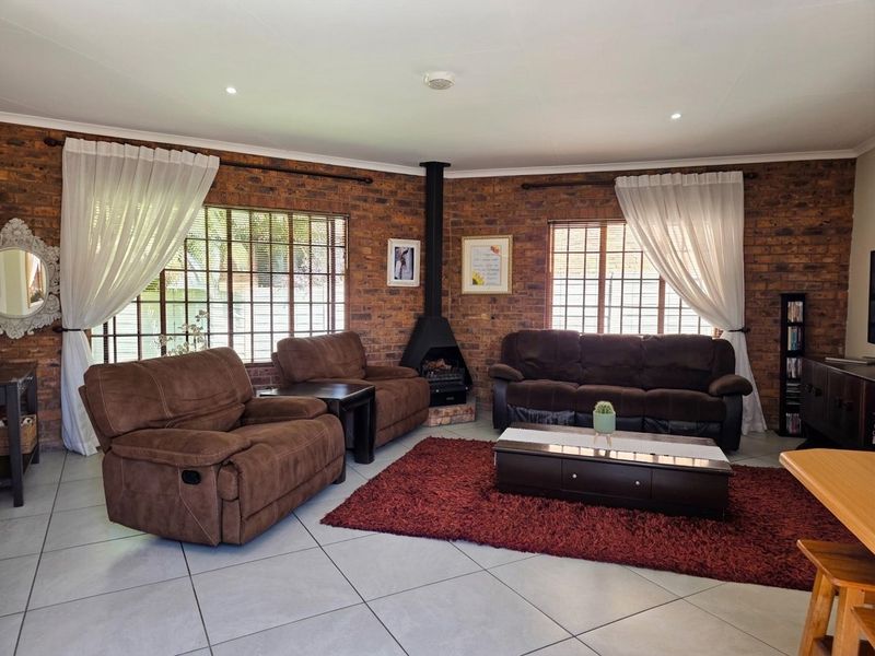 A spacious living room featuring exposed brick walls, a central freestanding fireplace, tiled flooring, and large windows allowing for natural light.