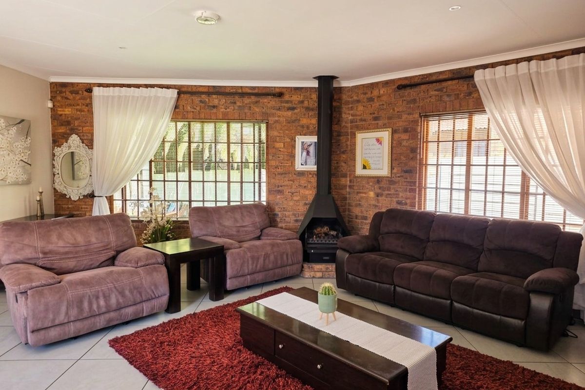A cozy living room featuring exposed brick walls, a central freestanding fireplace, tiled flooring, and large windows allowing for natural light.