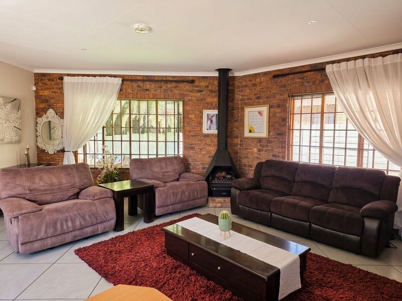 A cozy living room featuring exposed brick walls, a central freestanding fireplace, tiled flooring, and large windows allowing for natural light.