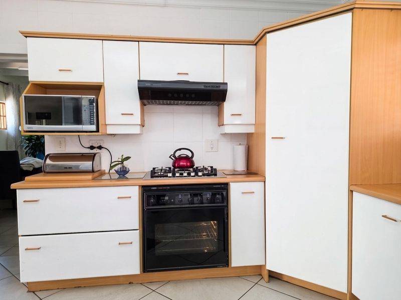 A functional kitchen featuring white cabinetry with wood-trim detailing, a built-in oven, gas hob, and tiled backsplash.