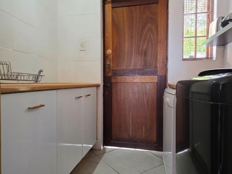 Functional laundry area featuring built-in cabinetry, laminate countertops, tiled splashbacks, and a solid timber door leading to the exterior.