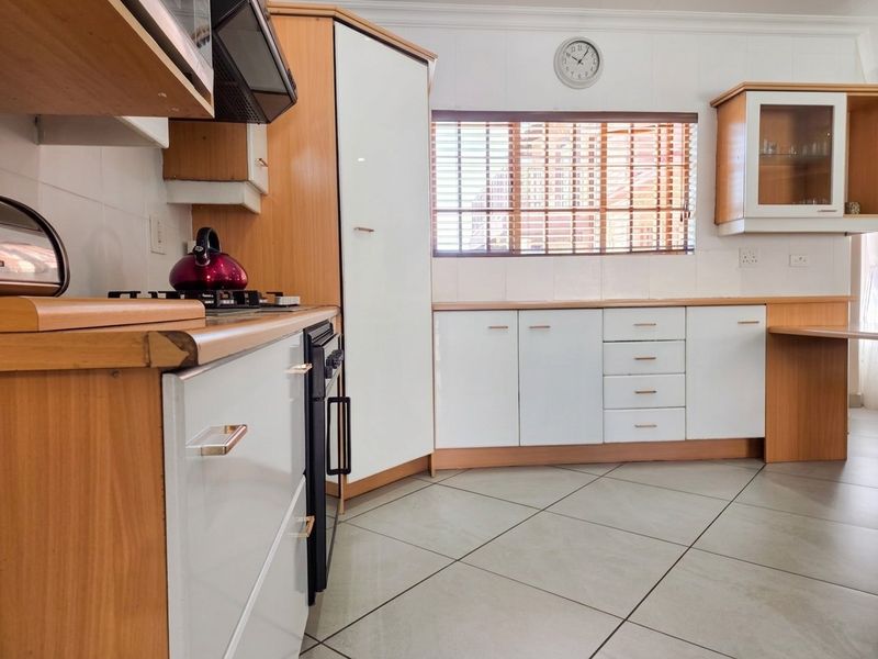 A functional kitchen featuring white and wood-veneer cabinetry, tiled flooring, a gas hob with extractor fan, and ample counter space.