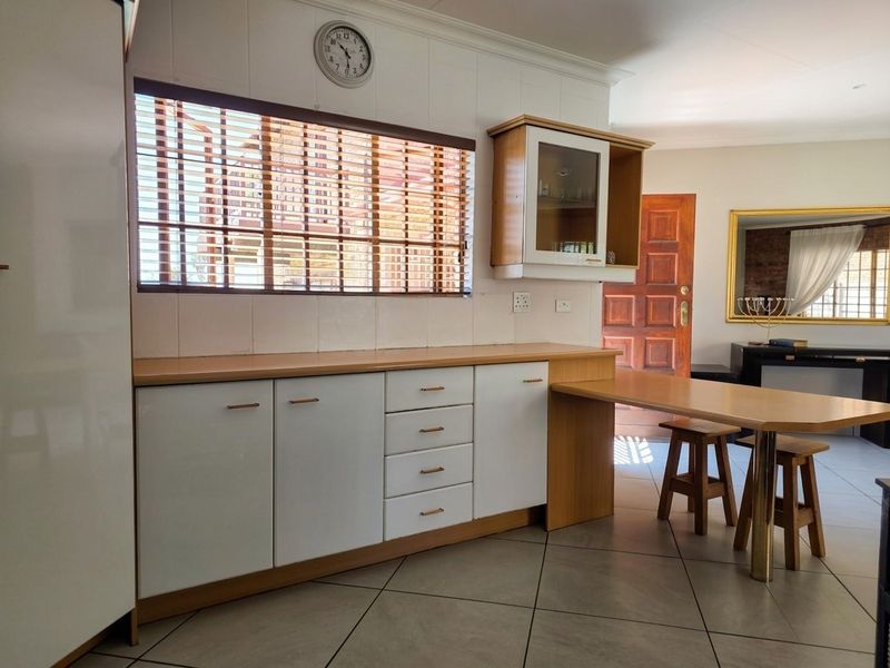 A functional kitchen area featuring white cabinetry, wood-tone countertops, a built-in breakfast bar, and tiled flooring with a neutral splashback.