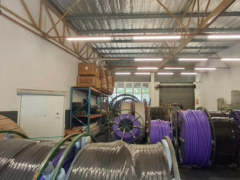 Industrial utility space featuring high ceilings with exposed steel trusses, roller shutter access, and functional overhead lighting, suitable for storage or light industrial operations.