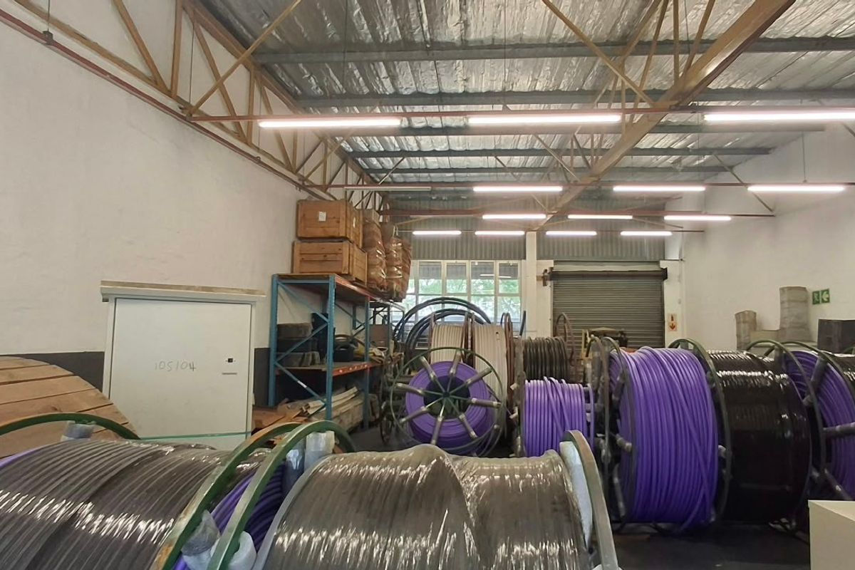 Industrial utility space featuring high ceilings with exposed steel trusses, roller shutter access, and functional overhead lighting, suitable for storage or light industrial operations.
