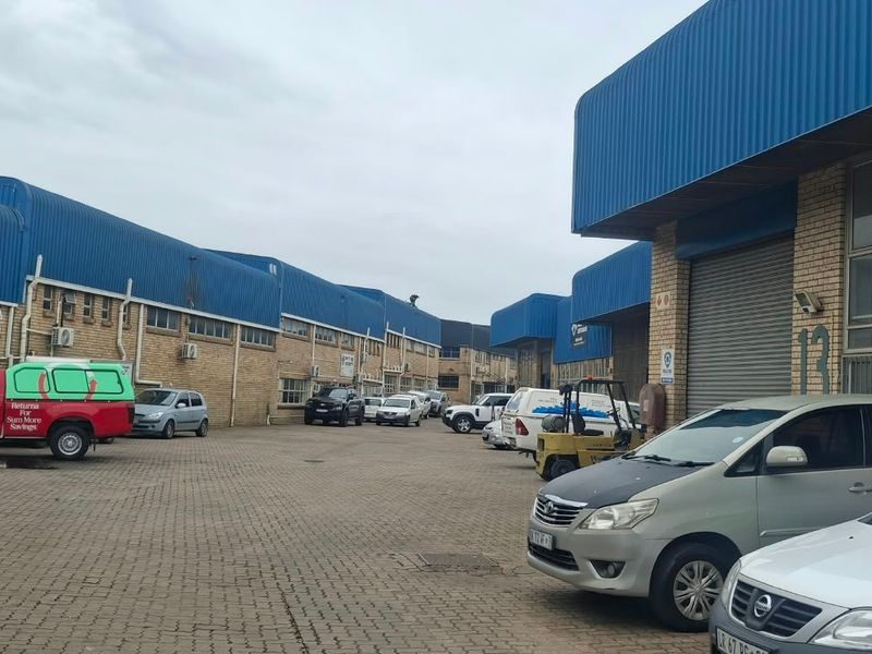 Exterior view of an industrial complex featuring face brick facades, blue corrugated metal roofing, and multiple roller shutter doors with a paved parking area.