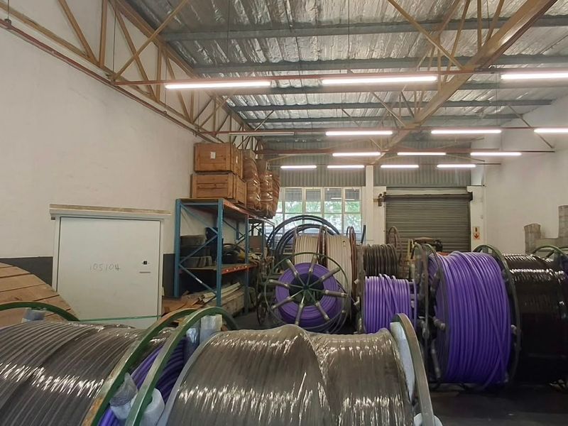 Industrial utility space featuring exposed steel roof trusses, roller shutter door access, and functional overhead fluorescent lighting, suitable for storage or workshop operations.