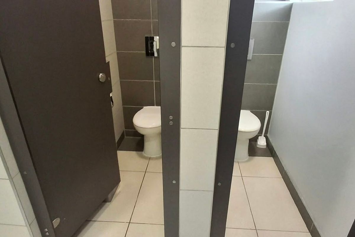 A functional office bathroom featuring two private toilet cubicles with tiled walls and flooring.
