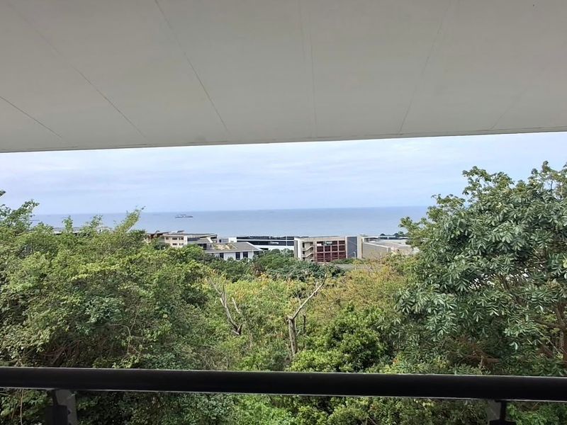 Elevated view overlooking lush greenery and distant coastal landscape from a balcony.