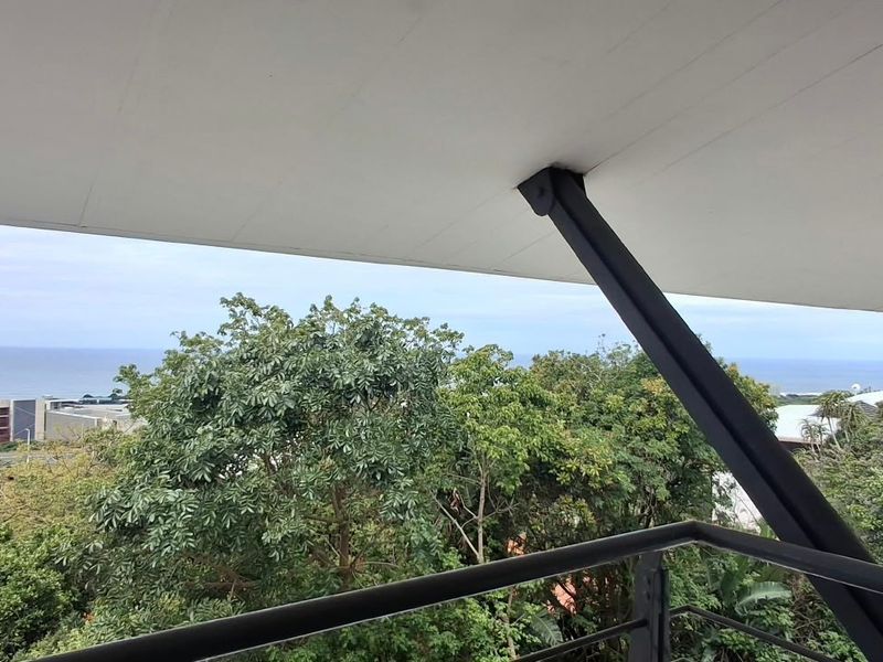 A modern balcony featuring a sleek overhanging roof, steel structural supports, and metal railings, offering expansive views of the surrounding landscape and ocean.