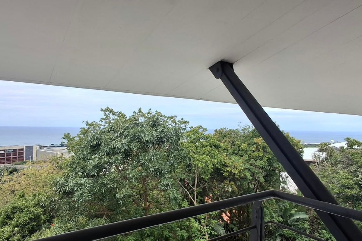 A modern balcony featuring a sleek overhanging roof, steel structural supports, and metal railings, offering expansive views of the surrounding landscape and ocean.