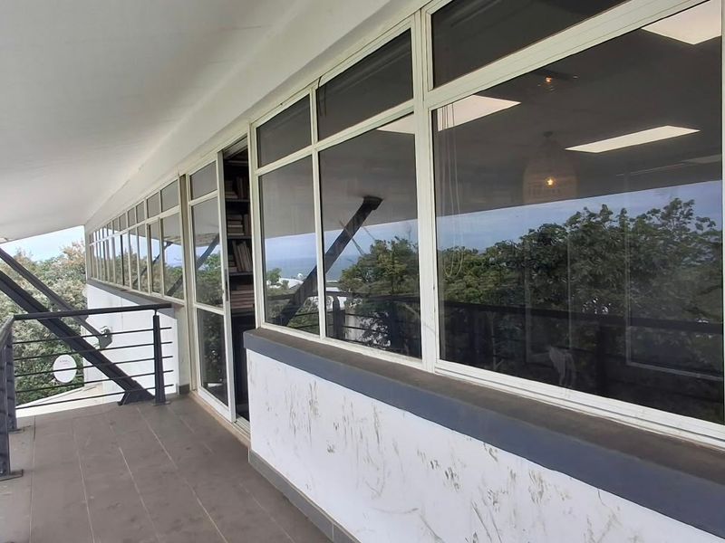 A spacious covered balcony featuring tiled flooring, metal railings, and large glass sliding doors providing access to the office interior.