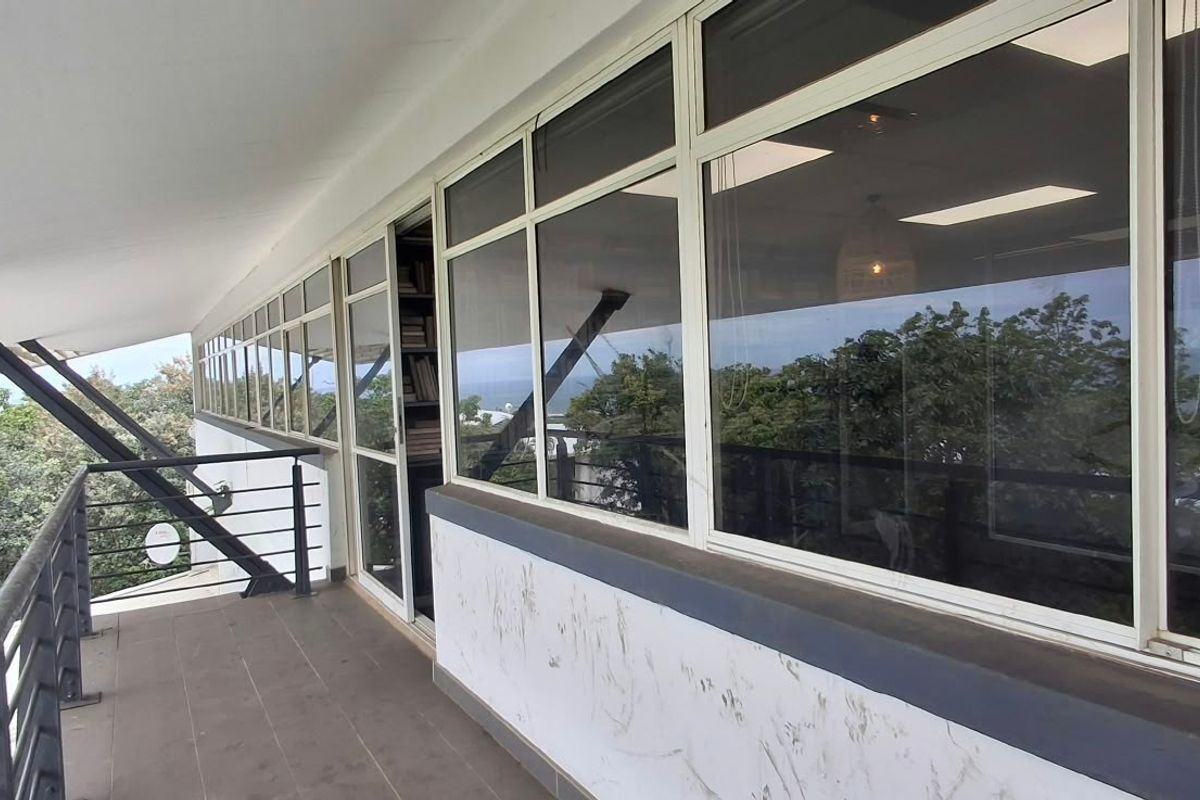 A spacious covered balcony featuring tiled flooring, metal railings, and large glass sliding doors providing access to the office interior.
