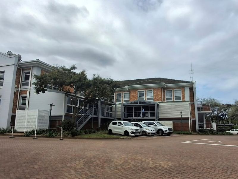 Exterior view of a multi-story office building featuring brick paving, a tiled roof, and external metal staircase access.
