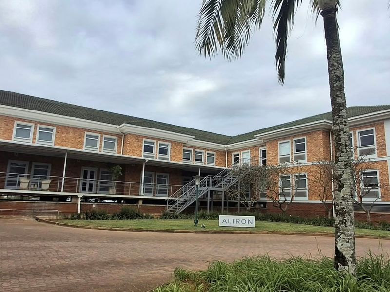 A professional office building featuring a brick facade, tiled roof, external metal staircase, and a paved driveway with landscaped surroundings.