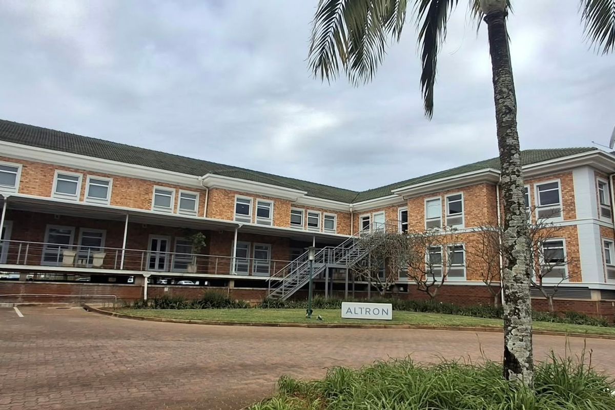 A professional office building featuring a brick facade, tiled roof, external metal staircase, and a paved driveway with landscaped surroundings.
