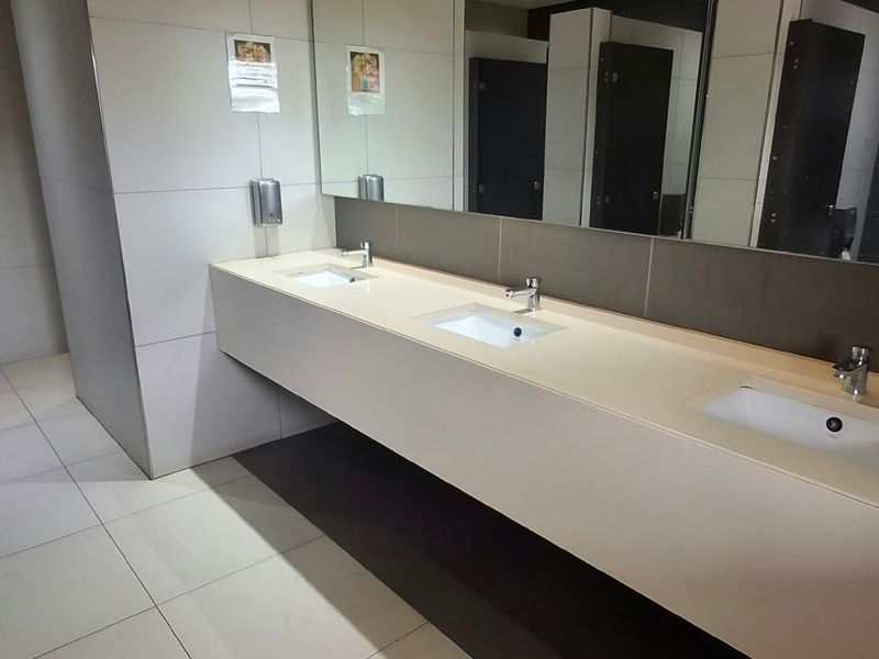 A clean, modern commercial bathroom featuring a triple vanity with integrated sinks, large wall mirror, and tiled finishes.