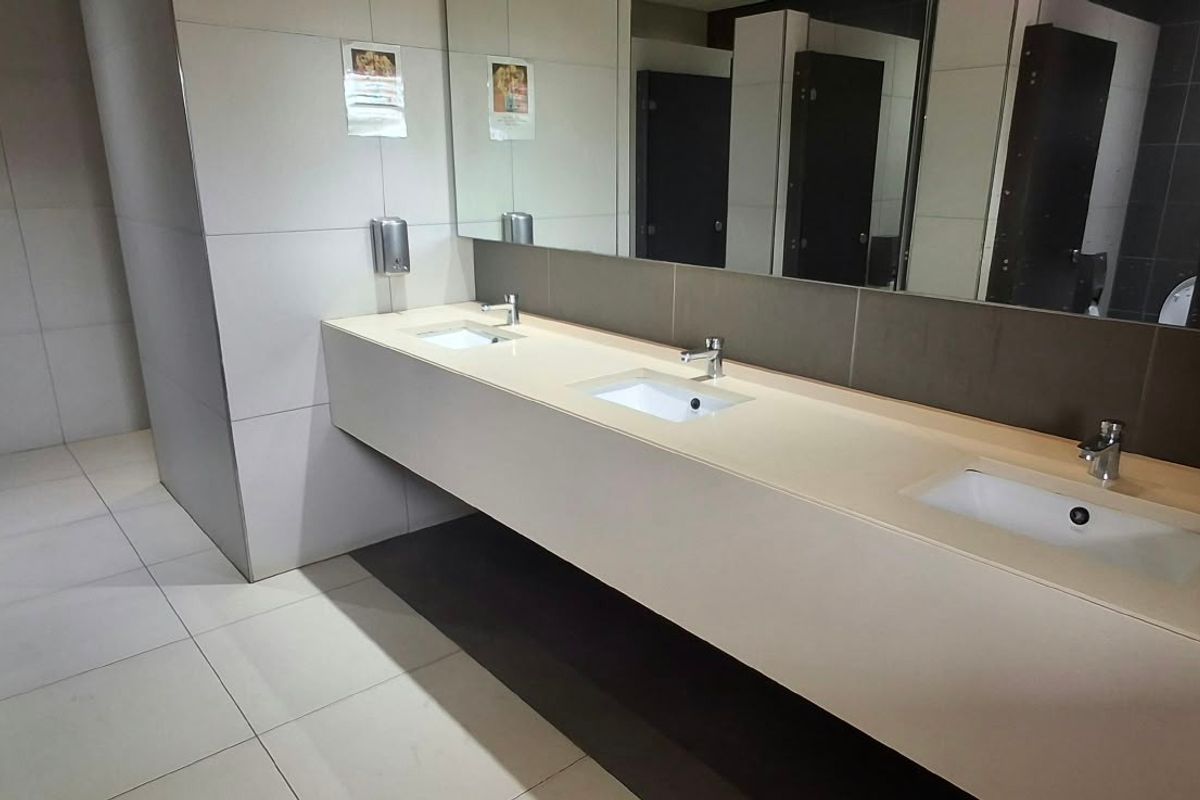 A clean, modern commercial bathroom featuring a triple vanity with integrated sinks, large wall mirror, and tiled finishes.