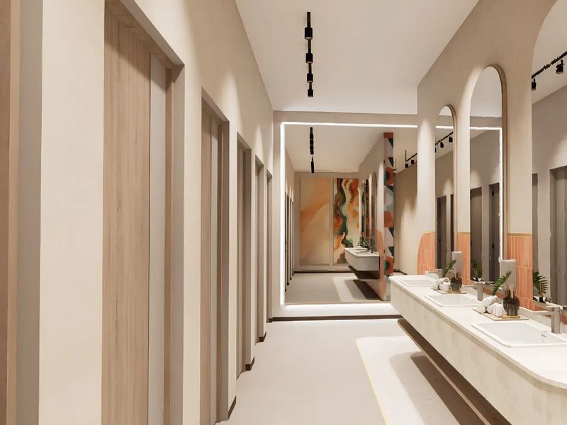 Modern office bathroom featuring a long integrated vanity with multiple sinks, arched mirrors, track lighting, and a clean, contemporary aesthetic.