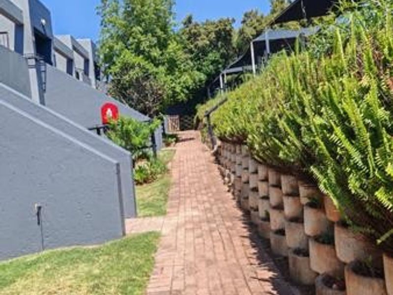 A well-maintained brick pathway leads through the rear garden area, featuring a structured retaining wall and established greenery.