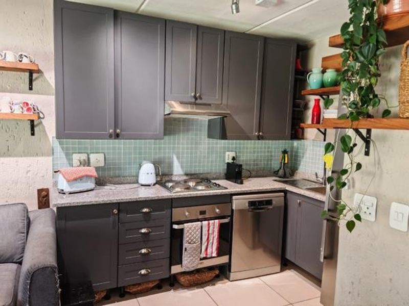 A compact kitchen featuring modern grey cabinetry, granite countertops, a mosaic tile backsplash, and integrated appliances including an oven, hob, and dishwasher.