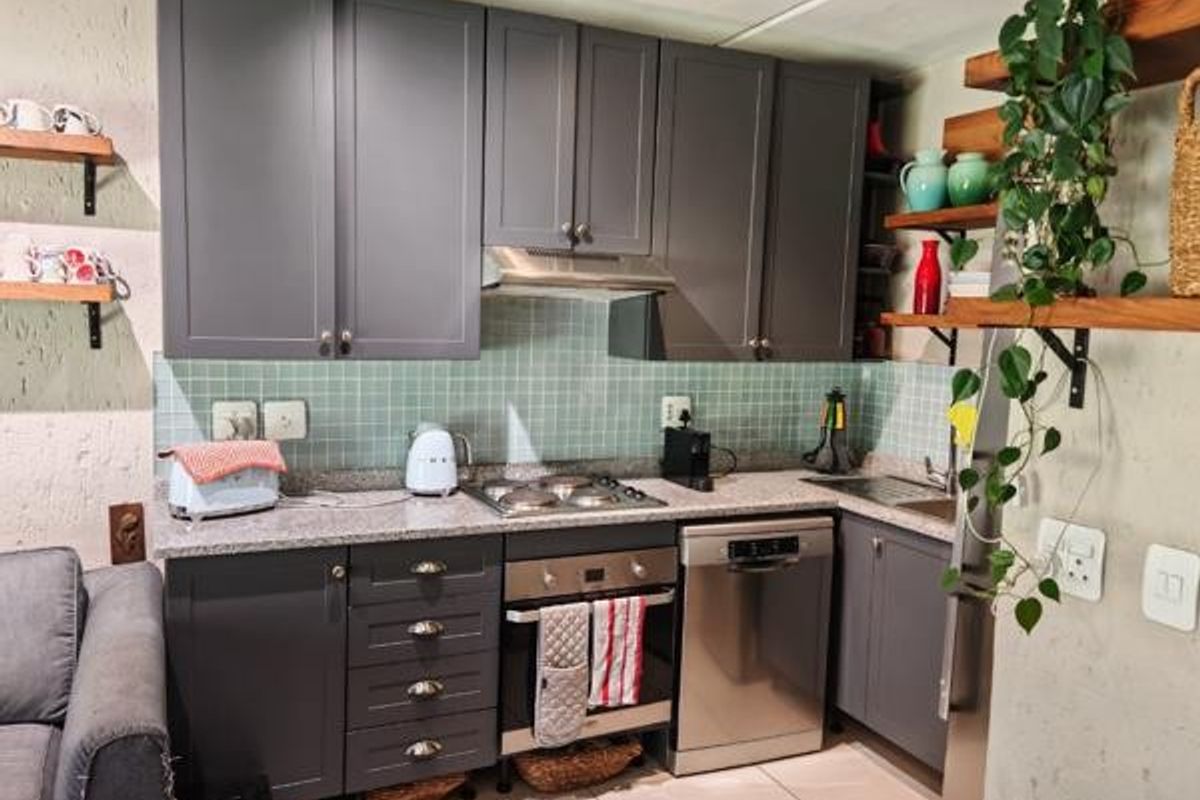 A compact kitchen featuring modern grey cabinetry, granite countertops, a mosaic tile backsplash, and integrated appliances including an oven, hob, and dishwasher.