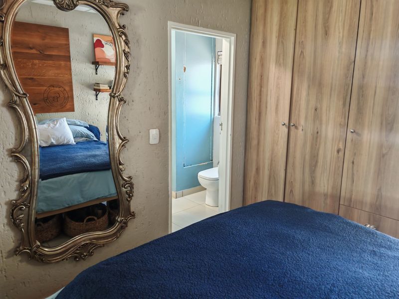 Bedroom featuring built-in wooden cupboards and textured walls, with an adjoining bathroom visible through the doorway.