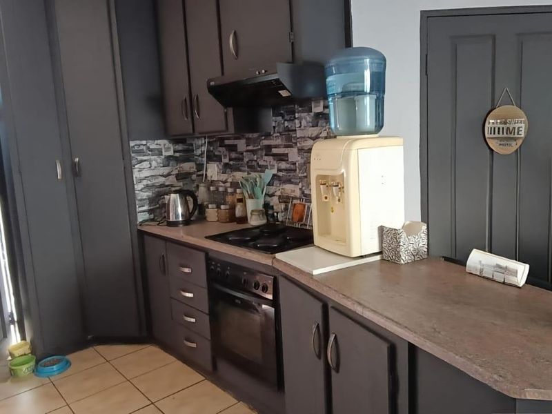 A functional kitchen featuring dark-toned built-in cabinetry, a laminate countertop, integrated oven and hob, and a tiled backsplash.