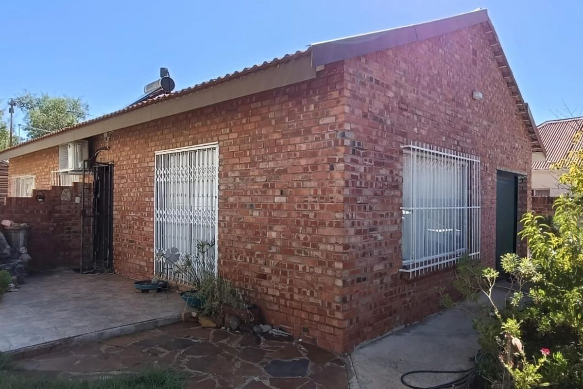Rear view of a face brick house featuring a paved patio area, security gates, and a solar water heater installation.