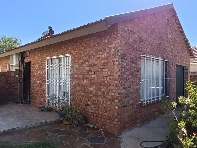 Rear view of a face brick house featuring a paved patio area, security gates, and a solar water heater installation.