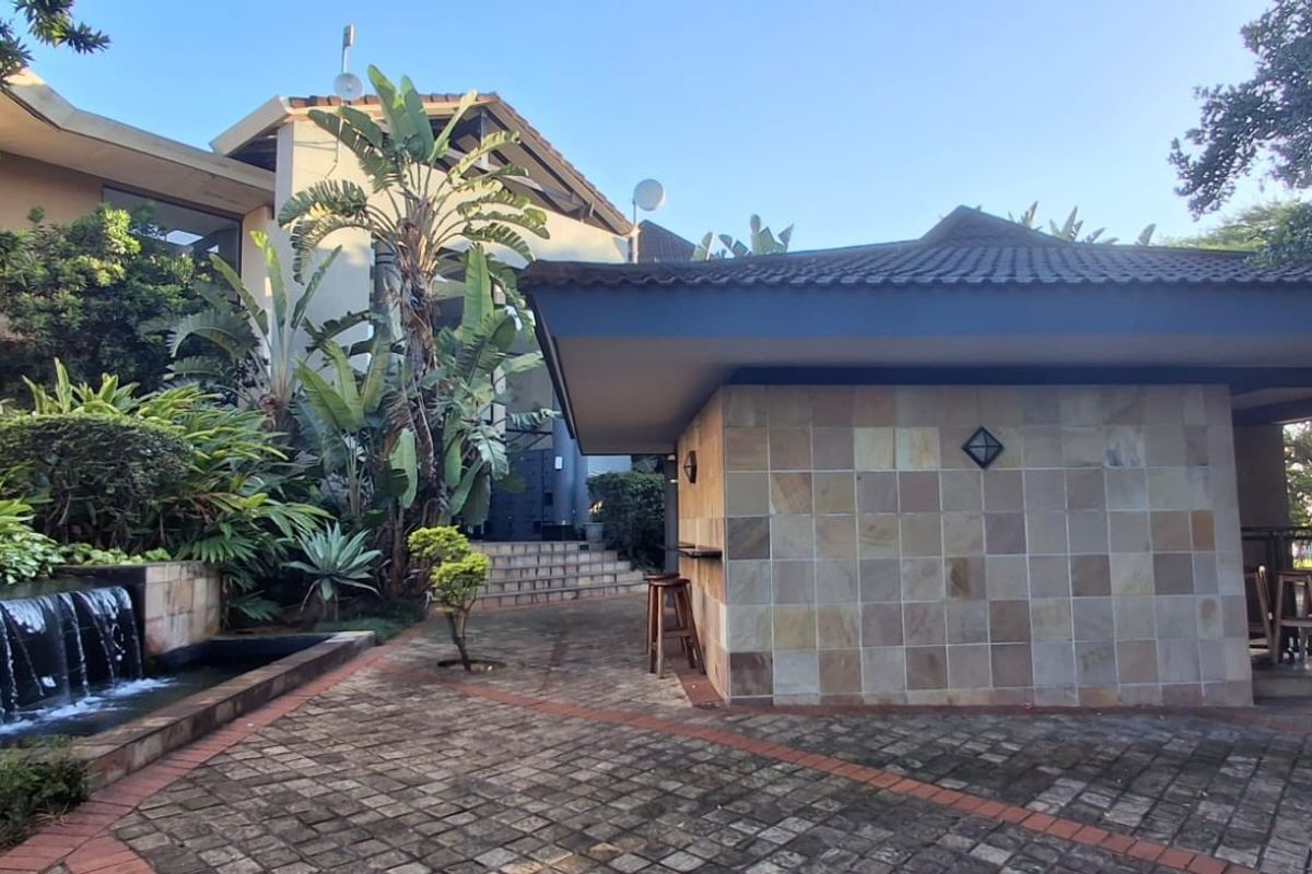 A well-maintained outdoor entertainment area featuring a stone-clad bar structure, paved courtyard, and a tranquil water feature set within a landscaped garden.
