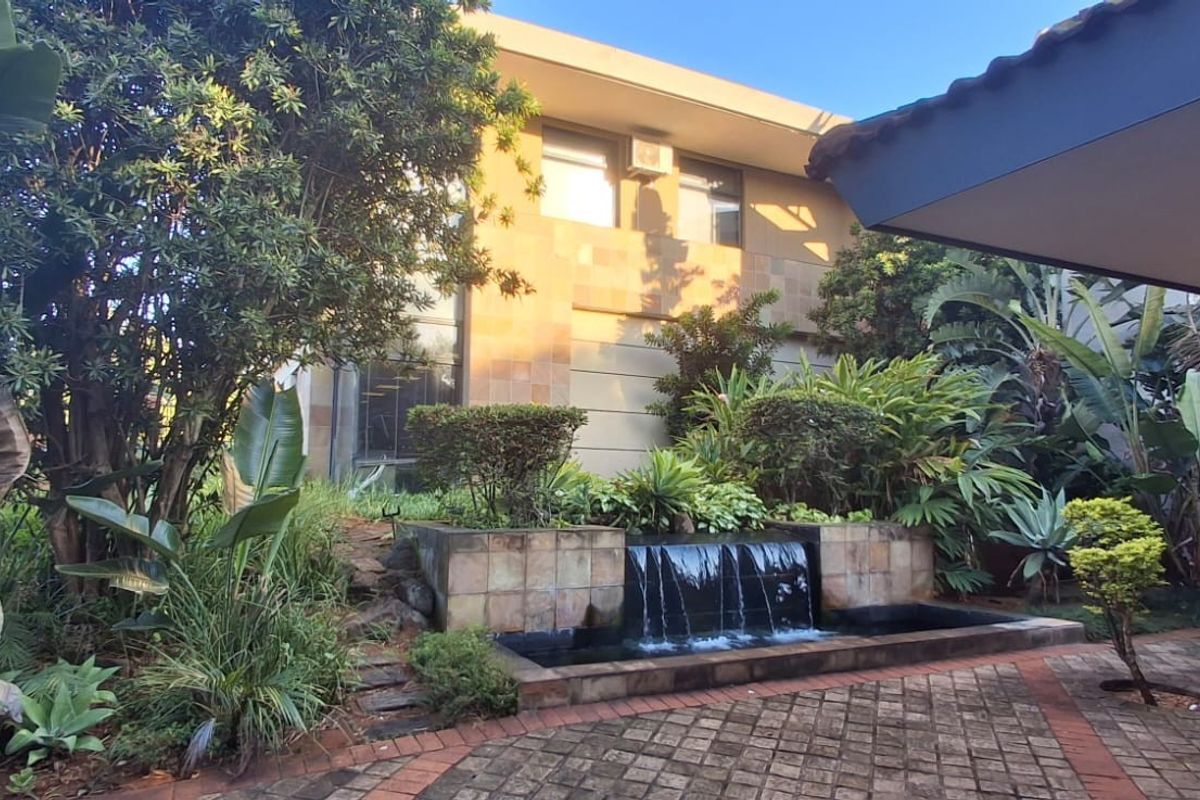 A well-maintained rear exterior area featuring a stone-tiled water feature, paved patio space, and established garden landscaping against the building facade.