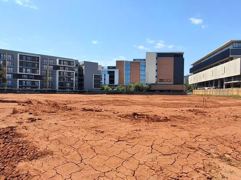 A vacant commercial land plot featuring cleared, level ground surrounded by modern multi-story commercial and residential buildings in a developed urban area.