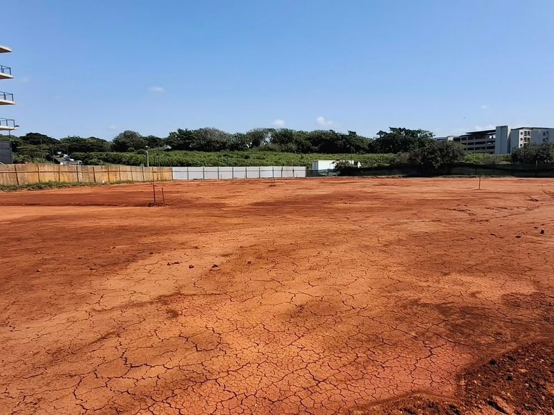 A wide-angle view of a cleared, vacant commercial land plot featuring perimeter fencing and surrounding urban development.