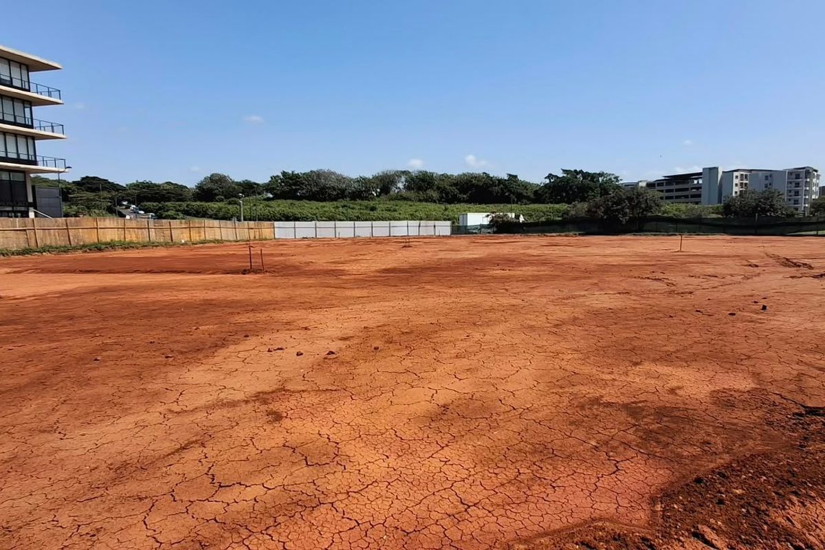 A wide-angle view of a cleared, vacant commercial land plot featuring perimeter fencing and surrounding urban development.